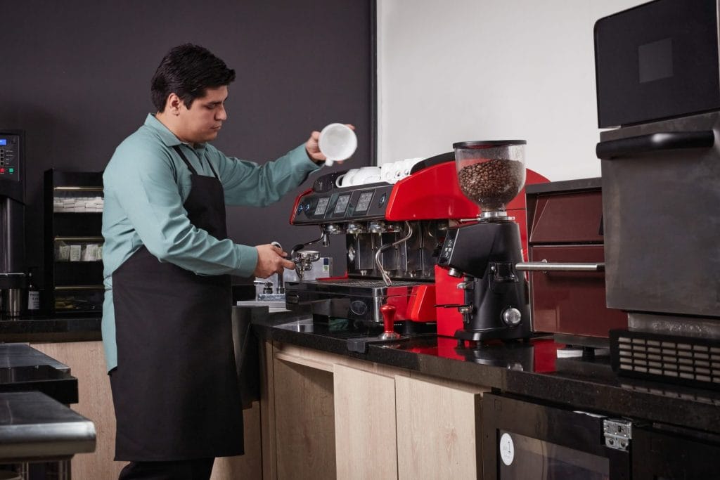 Barista wearing branded restaurant uniform apron preparing coffee behind the counter